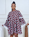Model wearing a short flared Ankara dress with white lace sleeve detailing in a minimalist living room setting.