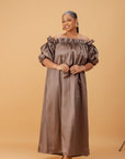 Woman wearing an off-shoulder brown maxi dress with puff sleeves and a flowing ankle-length design on a neutral background.