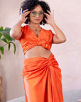 Woman wearing an orange satin crop top and matching ruched skirt, styled with statement glasses