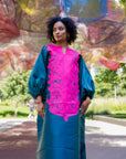 Model wearing luxurious teal Boubou dress with bold pink embroidery and voluminous sleeves.