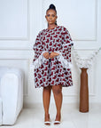Model wearing a short flared Ankara dress with white lace sleeve detailing in a minimalist living room setting.