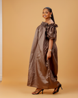Woman wearing an off-shoulder brown maxi dress with puff sleeves and a flowing ankle-length design on a neutral background.