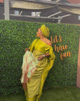 Elegant woman in a gold Show Stopper Boubou with draped detailing, posing gracefully at an outdoor event.