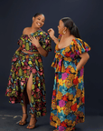 women wearing a vibrant floral maxi dress with puff sleeves, a front bow detail, and side pockets against a dark background.