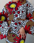 Woman wearing a bold Ankara two-piece set with flared sleeves and a fitted skirt in red, yellow, and black floral prints.