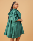 Model wearing an emerald green satin bow sleeve dress with voluminous sleeves and structured bow detail on the shoulder.
