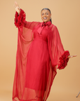 Model wearing a red organza statement dress with bow-tie neck and textured floral sleeve details, styled for formal and festive occasions.
