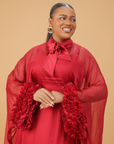 Model wearing a red organza statement dress with bow-tie neck and textured floral sleeve details, styled for formal and festive occasions.
