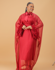 Model wearing a red organza statement dress with bow-tie neck and textured floral sleeve details, styled for formal and festive occasions.
