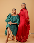 Model wearing an emerald green satin bow sleeve dress with voluminous sleeves and structured bow detail on the shoulder.
